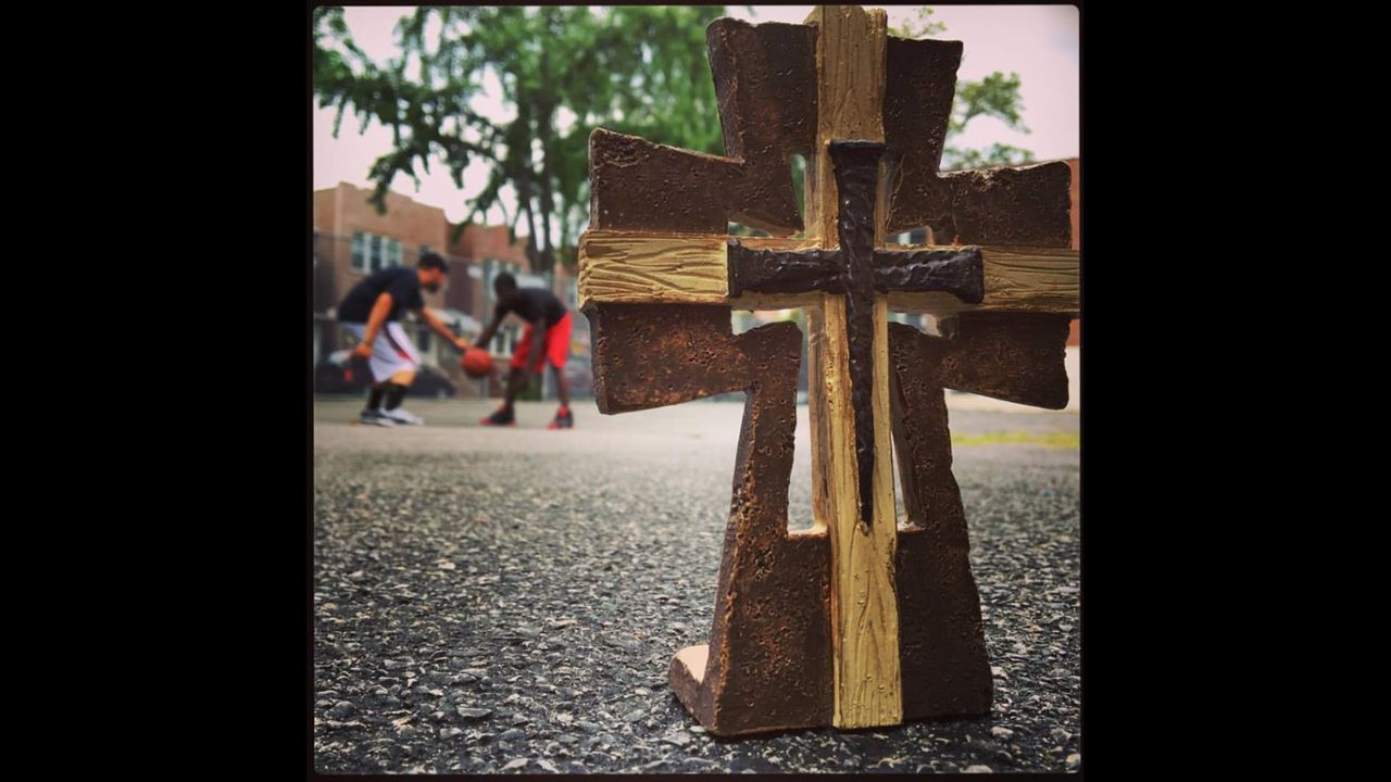 A wooden and iron cross outside Trinity, with children playing on the basketball court beyond