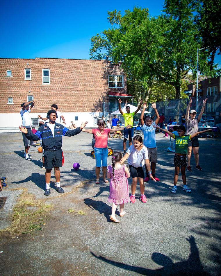 Neighbours and children with arms outstretched at a block party on Trinity’s lot, the church building behind them